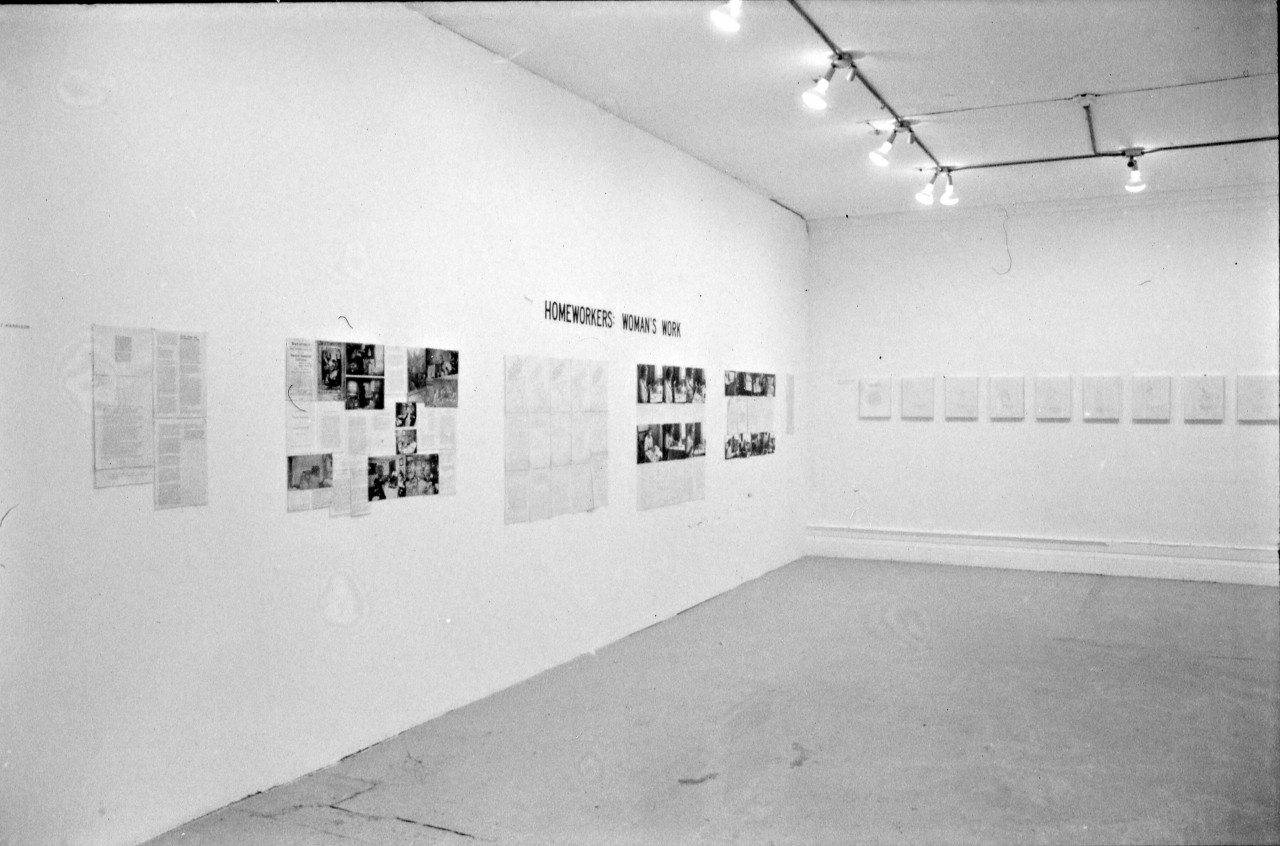 Photograph of two white gallery walls. On one wall there are photographs, text, and the title "HOMEWORKERS: WOMAN