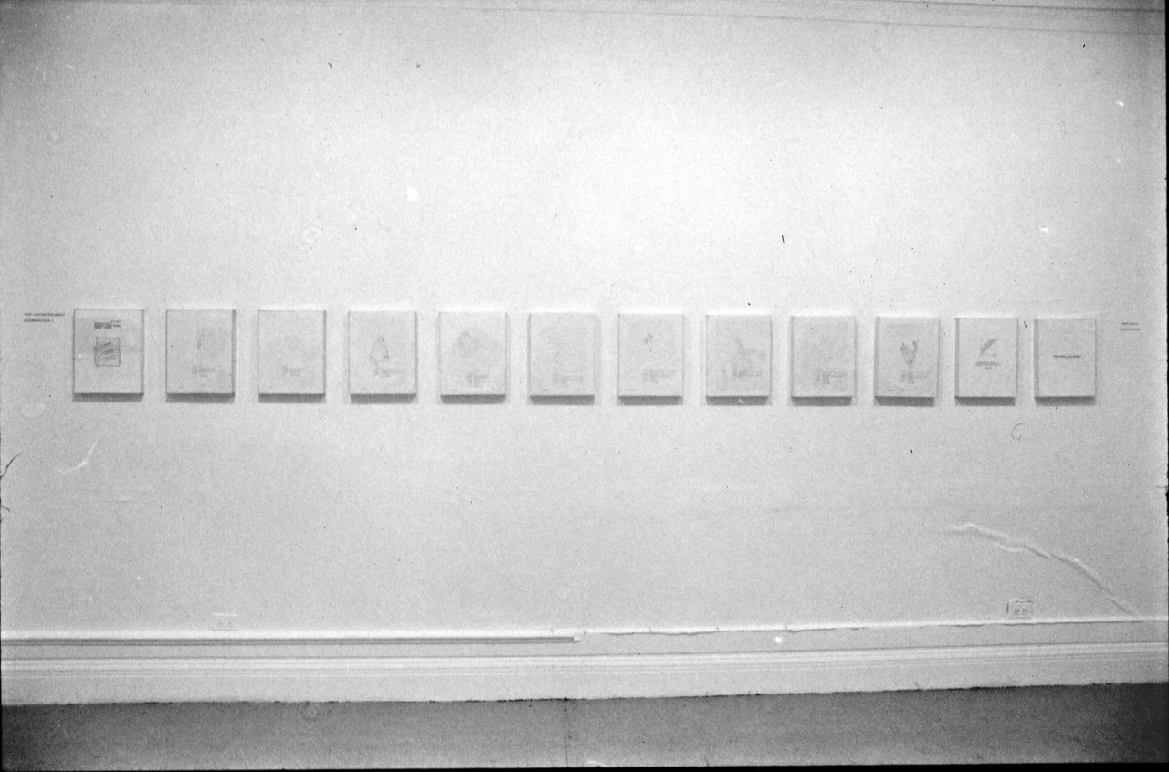 A photograph of a white wall hung with 12 works of the same size in a row.