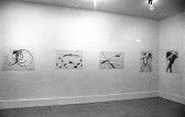 Various drawings are hung up on white walls. The drawings consist of simple shapes and lines.