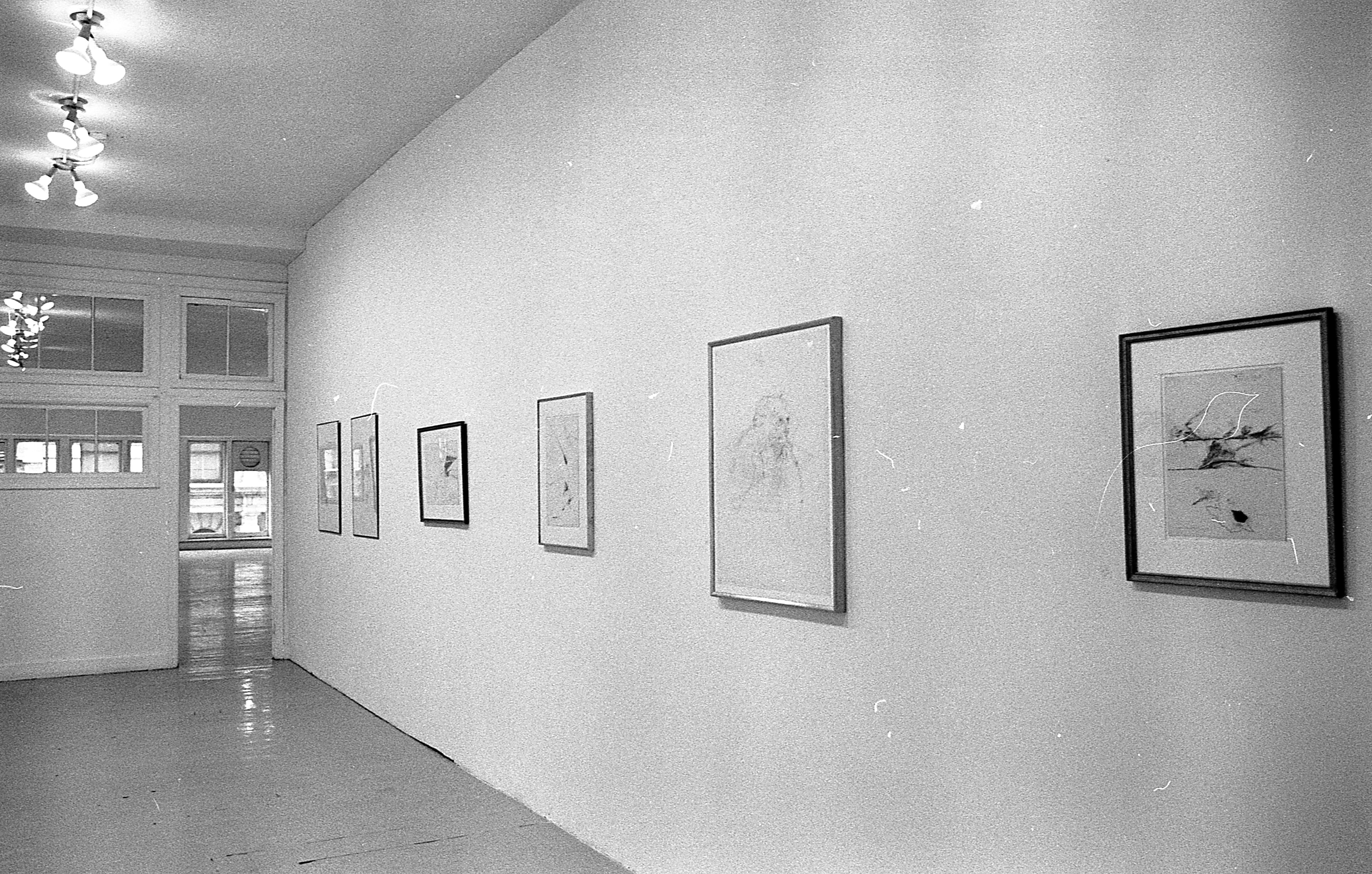 Six framed drawings are hung in a row on a white wall.