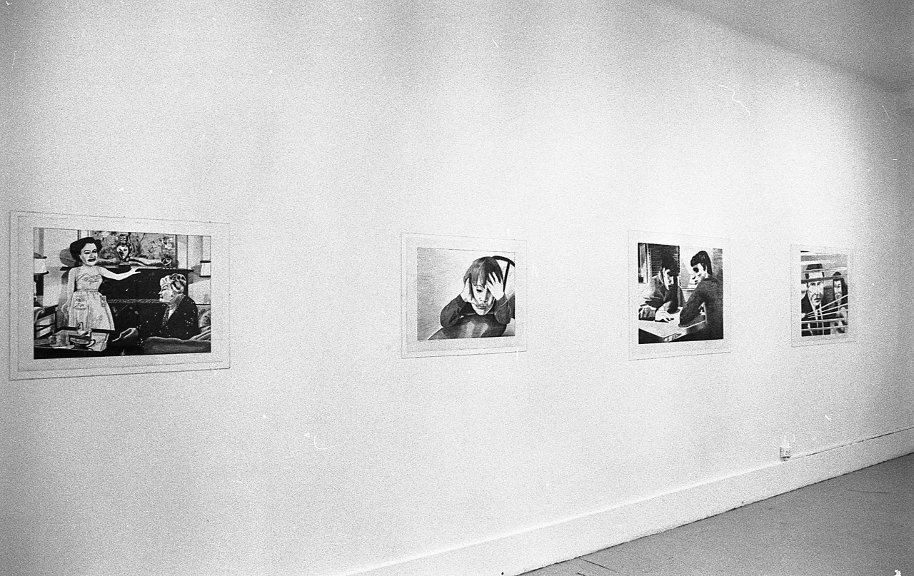 Four drawings are hung in a row on a white wall. The leftmost drawing shows two women sitting in a living room. The next shows a figure holding their head in their hands. The next depicts two men sitting at a table. The drawing on the far right depicts a man and a woman looking out a window through window blinds.