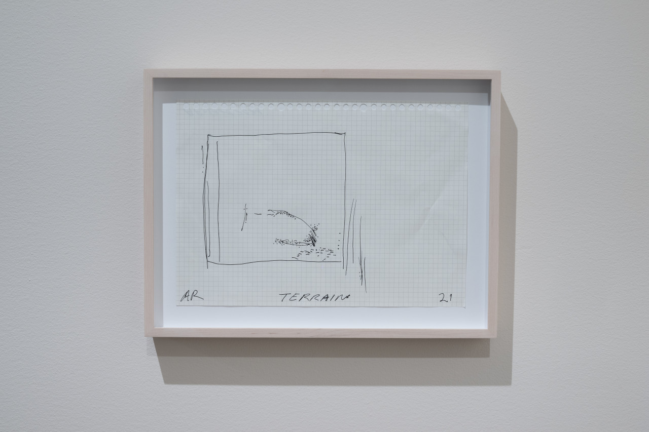 Color image of a framed piece of notebook graph paper, with a pen and ink drawing of a rectangle with various lines and dots. In the bottom-center of the paper is the word "TERRAIN."