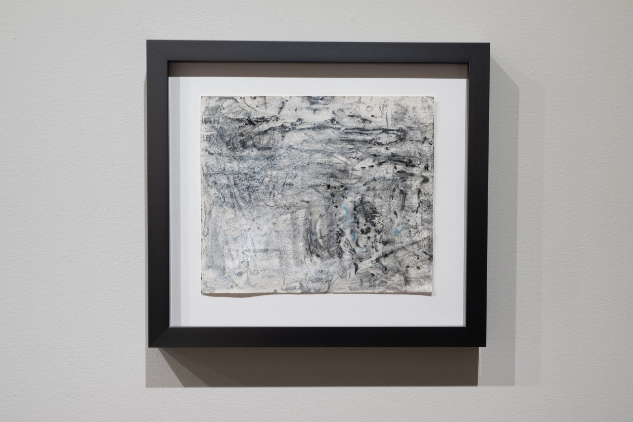 Color image of a framed work of black graphite on paper. Black lines run throughout the composition, with a layer of white bumps creating a textured surface over the top, small patches of blue accent the piece.
