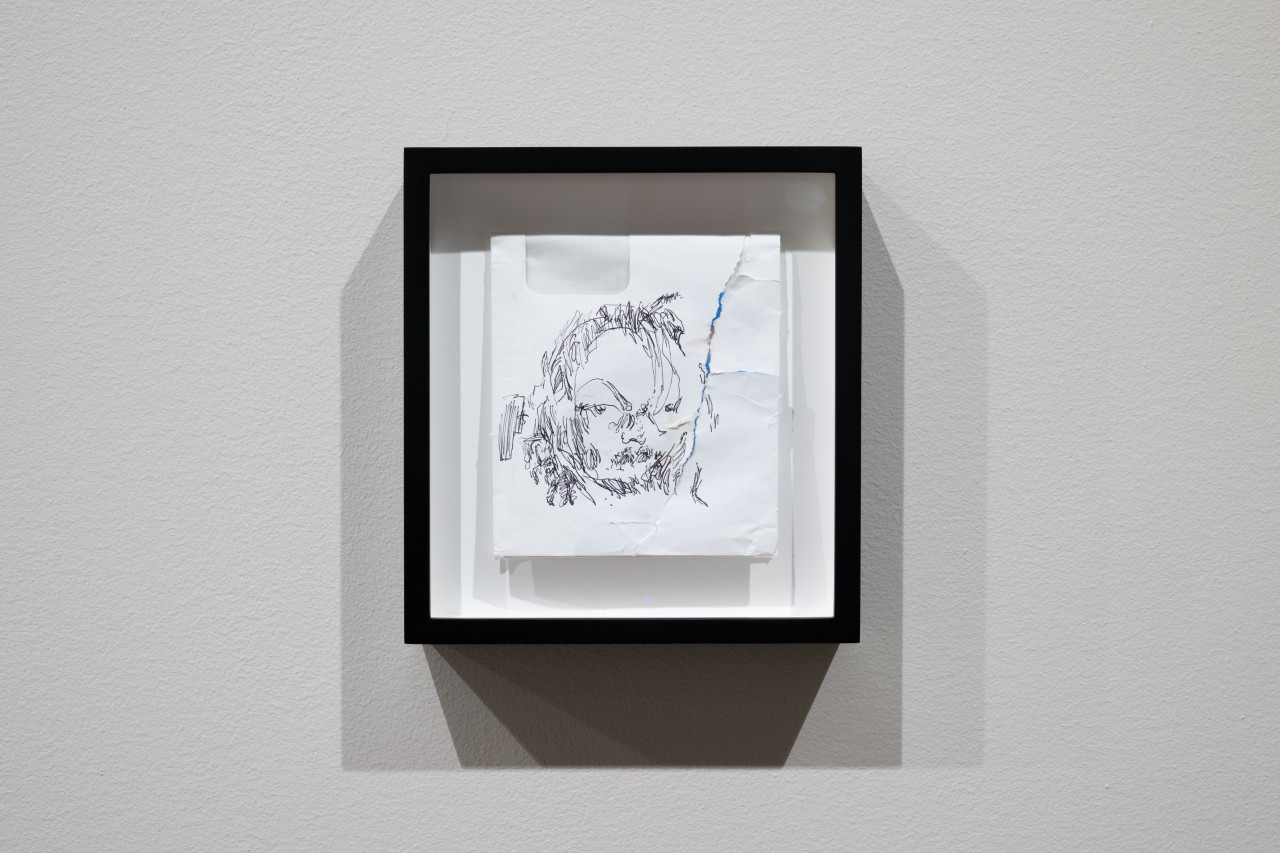 Color image of a small framed white envelope, folded in half, with an abstract pen drawing of a face on it.