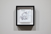 Color image of a small framed white envelope, folded in half, with an abstract pen drawing of a face on it.