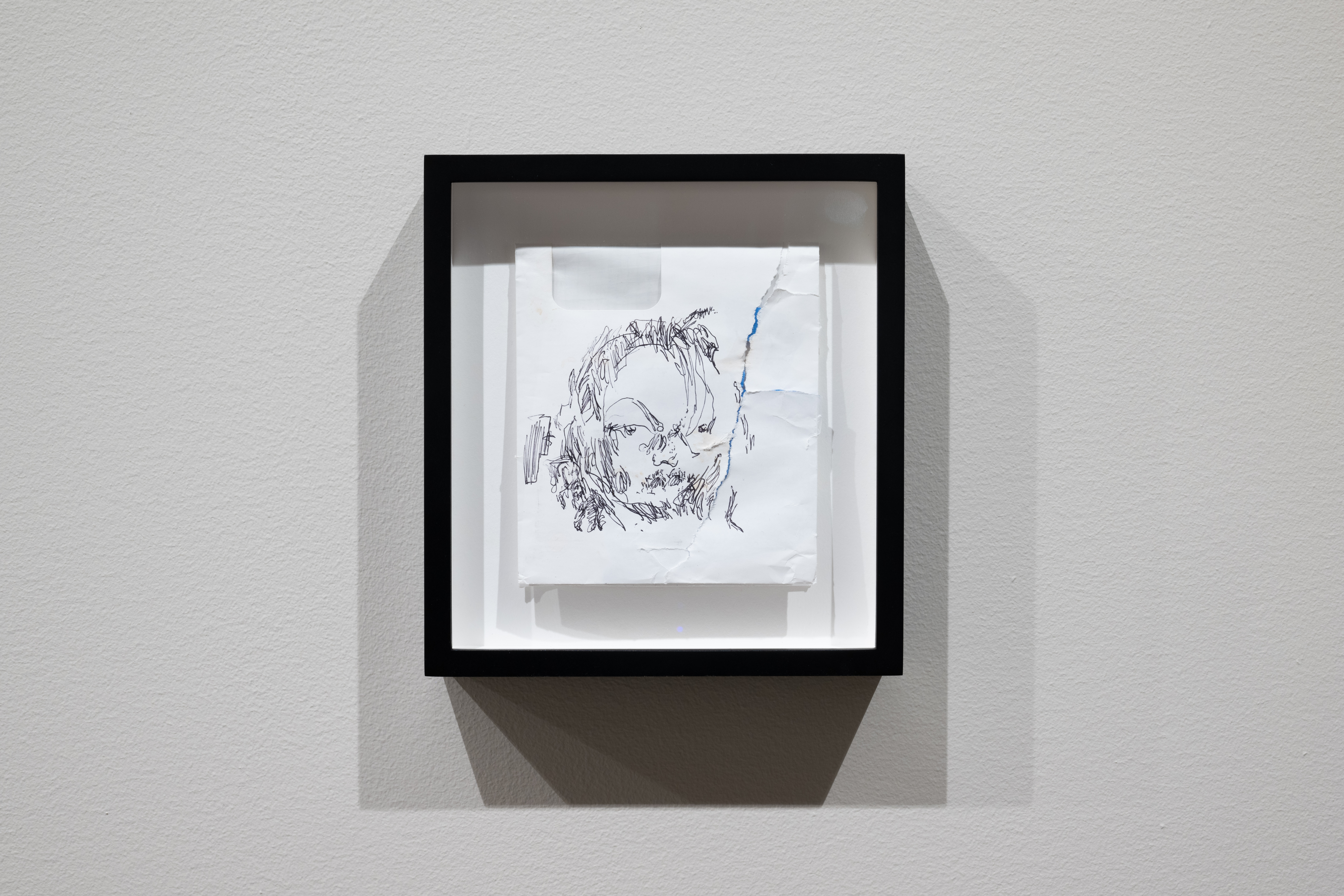 Color image of a small framed white envelope, folded in half, with an abstract pen drawing of a face on it.