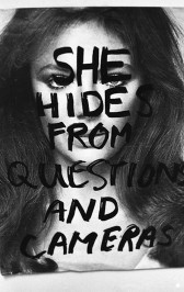 A black and white photograph of a figure with long dark hair. Over the figure's face the words 