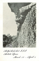An image of rocky terrain with a cliff in the forefront. Near the lower left corner of the photograph are some shrubs and a tiny human figure in the distance. Below the image is text reading: 