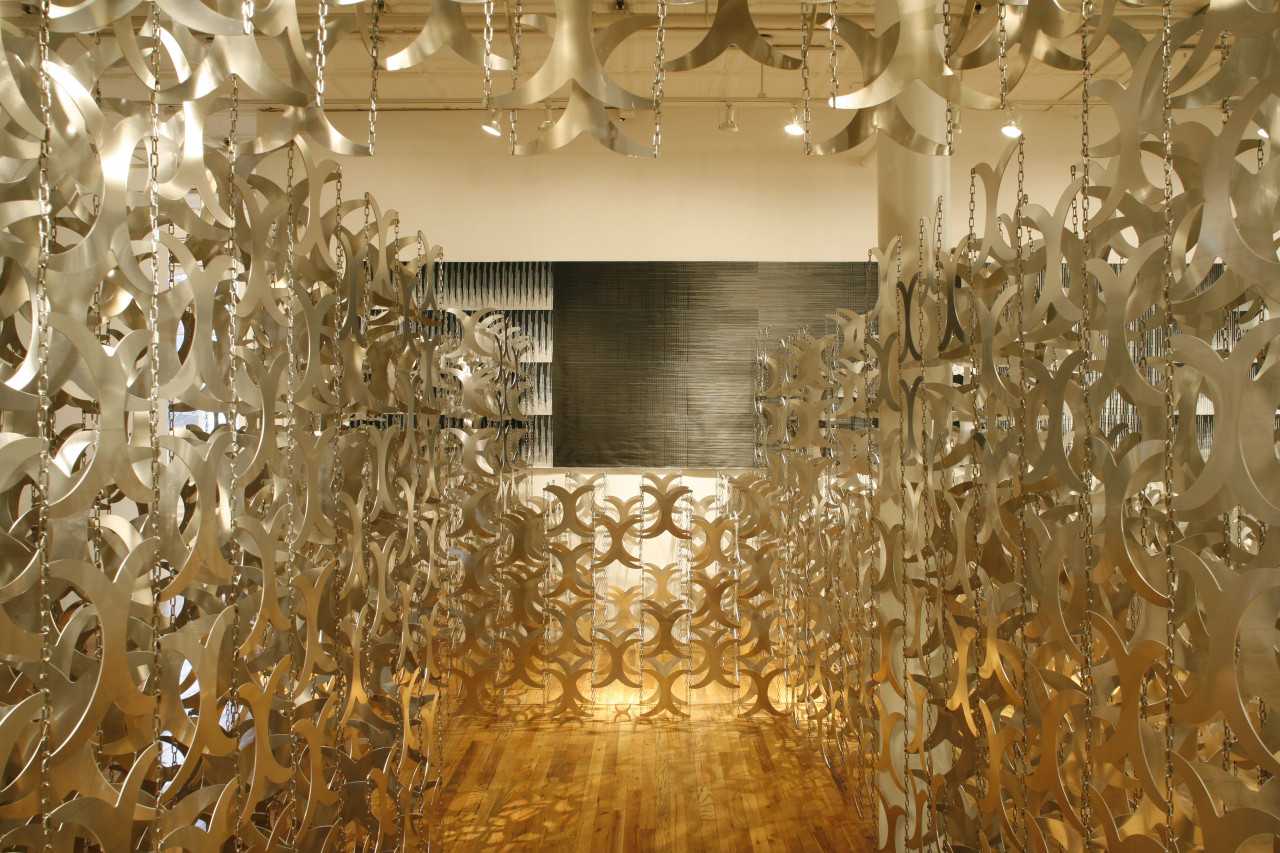 A large gallery space full of hundreds of metal cutouts shaped like curved "x"