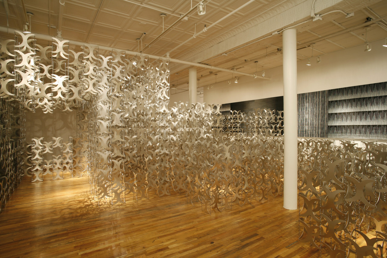 A large gallery space full of hundreds of metal cutouts shaped like curved "x"