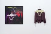 An image of a wall with a poster hanging on the left, and and a brown and white jacket hanging on the right.