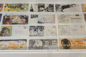 A close-up of a vitrine housing several postcards which have been drawn and collaged upon.