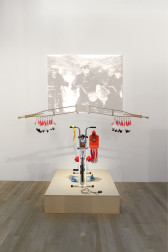 An image of a sculpture made out of bicycle parts, as well as other materials. Behind the sculpture is a projection.