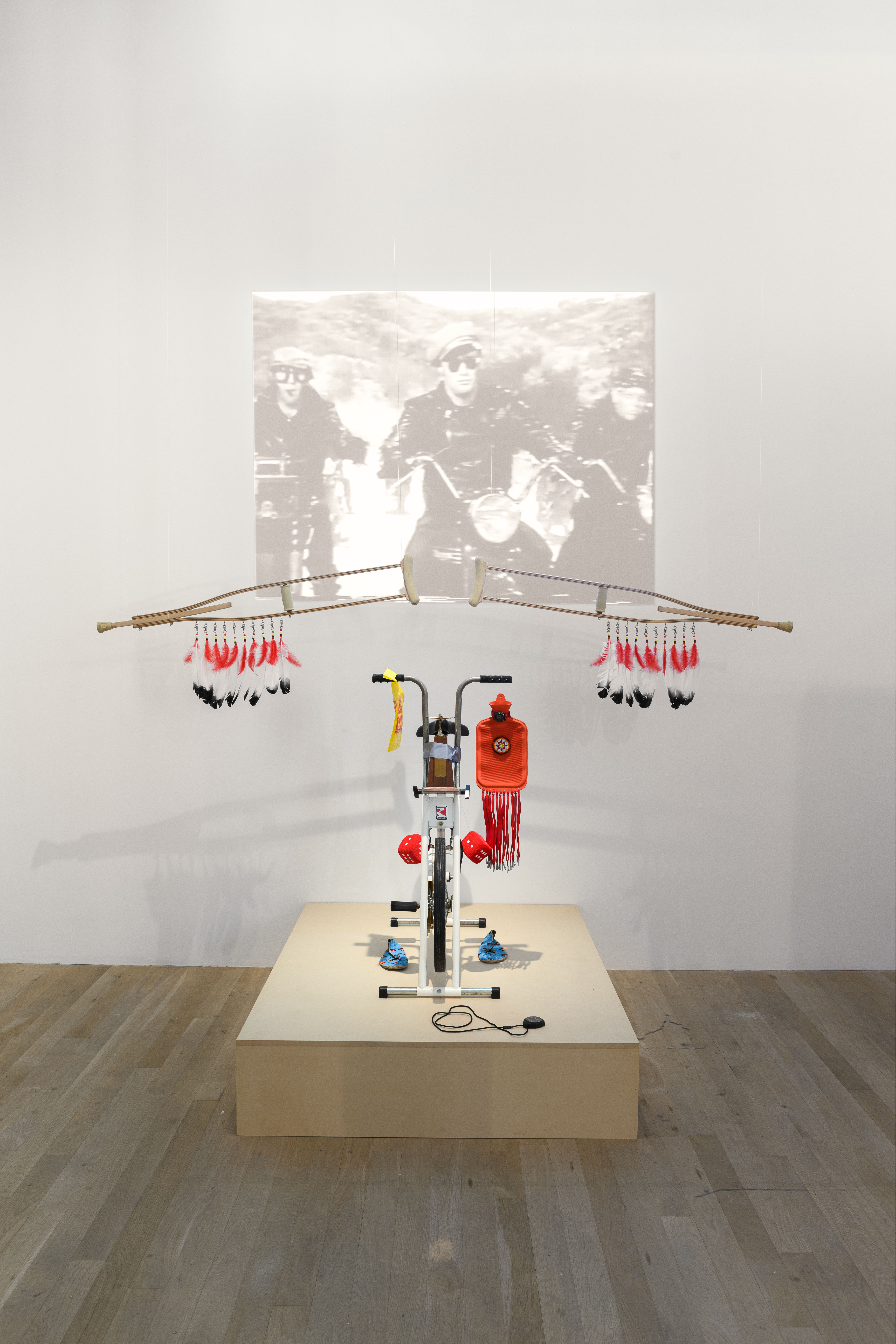 An image of a sculpture made out of bicycle parts, as well as other materials. Behind the sculpture is a projection.