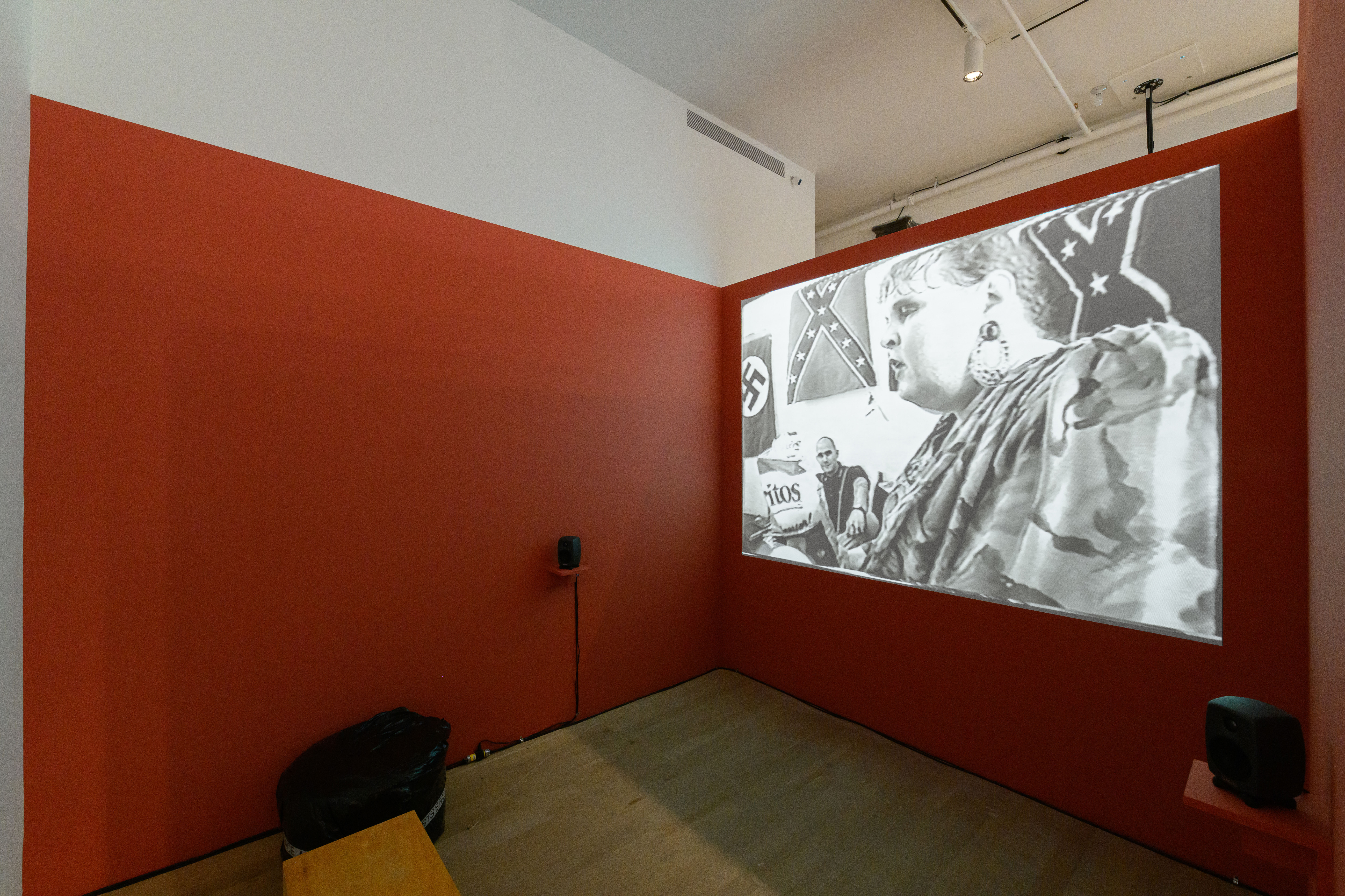 An image of a gallery space with walls painted red and a projection with speakers in front of the right-facing wall.