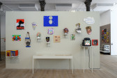 An image of a wall mounted with various colorful masks and cardboard paintings. Below them is a glass display case.