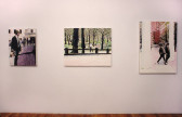 Three paintings arranged in a horizontal line on a white wall. Each painting depicts a man walking on city streets or in a park.