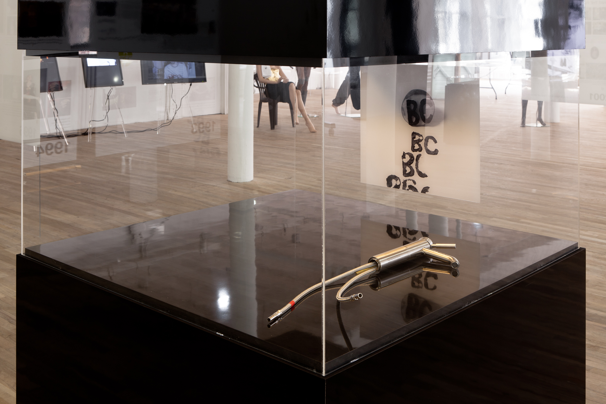 Detail view of a display case. It is mostly empty, save for a metal gun-type object with two small pipes extending out of the nozzle, and a poster with the repeated letters 