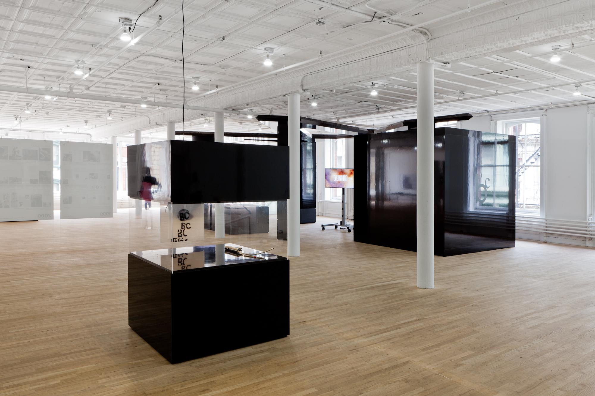 A large display case whose top and bottom portions are made of a shiny, black material. Held between these black components is a glass vitrine that displays several objects, including a flat surface covered with inky text that reads, 