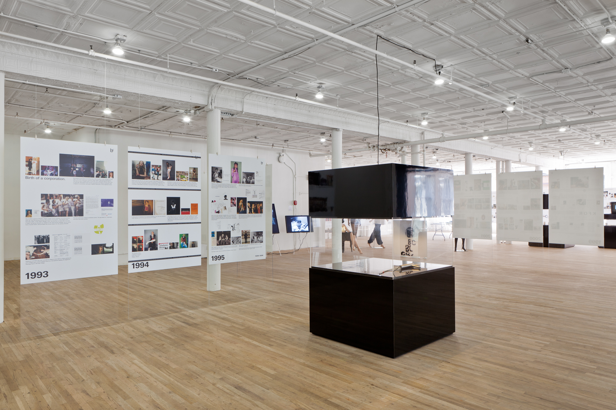 Overview of a gallery space depicting three plexiglass timelines, 1993-1995, and one black display case.