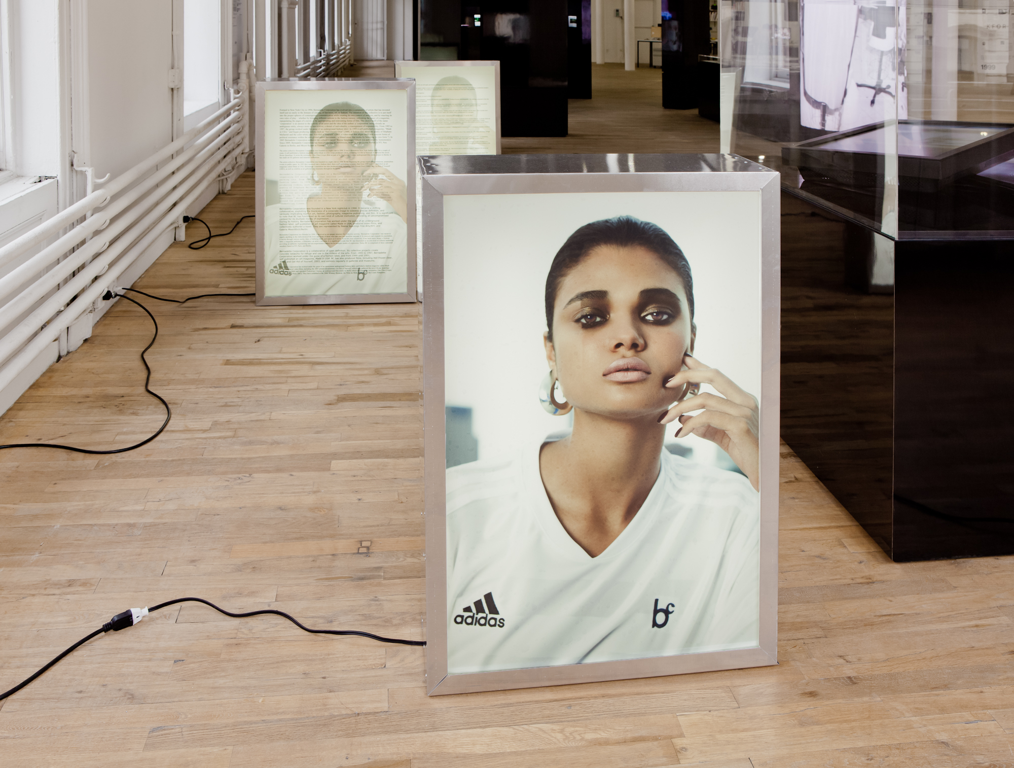 Three floor-standing, backlit images of a woman wearing a white Adidas soccer jersey decorated with a 