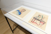 A close up image of a glass display case holding artworks in gouache and watercolor.