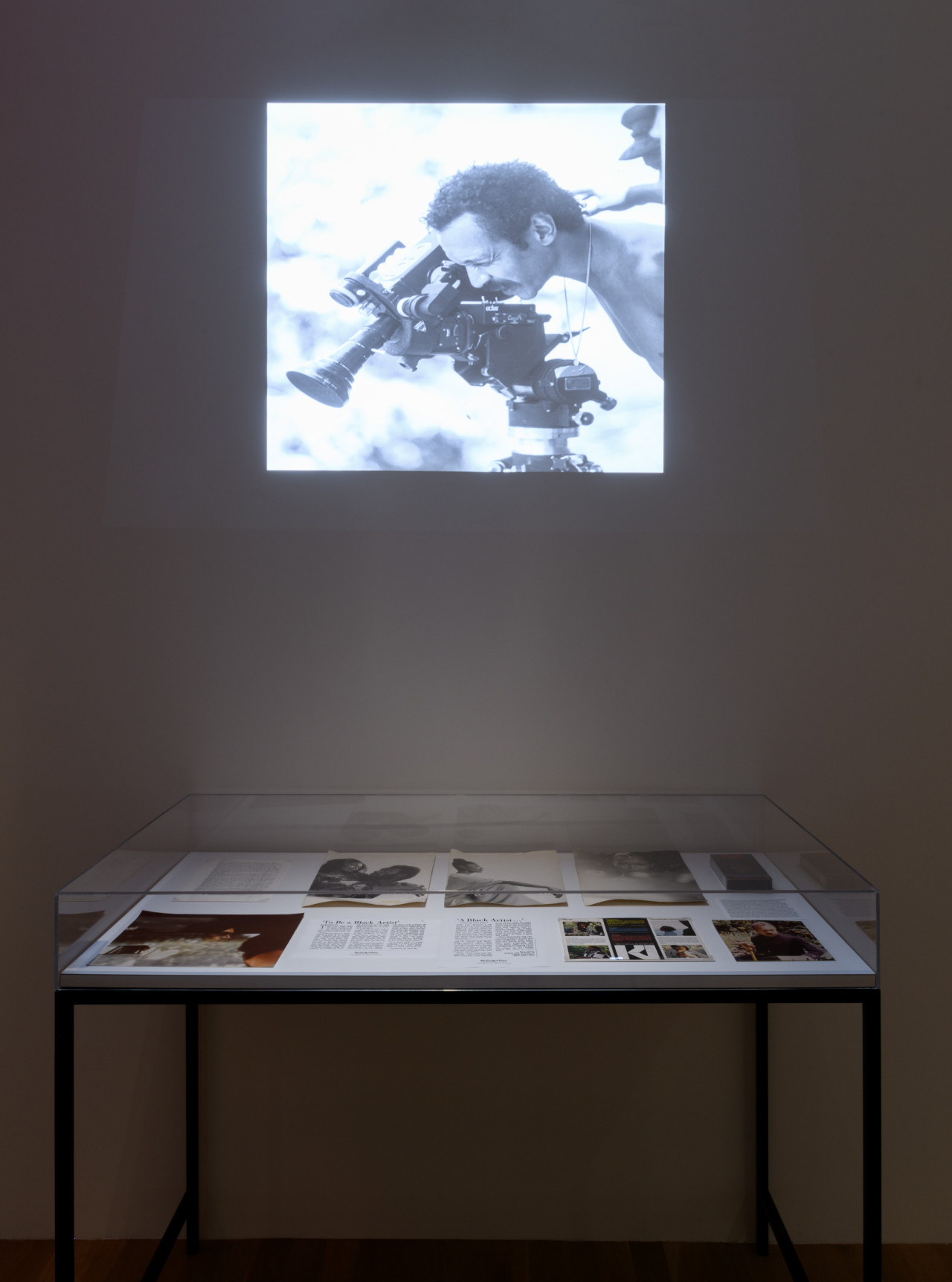 An image of a projection in a dark room above a glass display case holding ephemera.