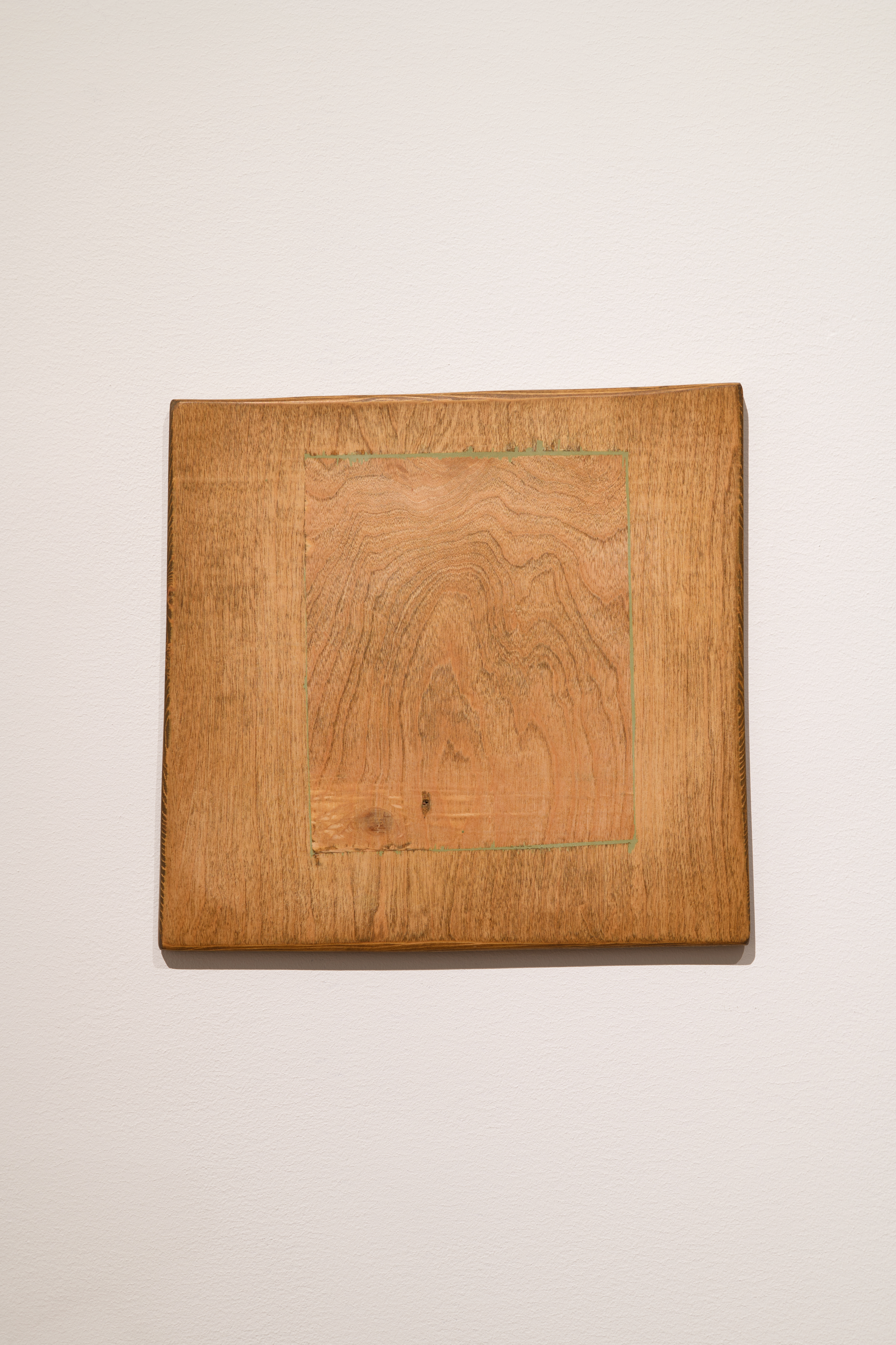 A smaller wooden panel has been inserted into a larger surrounding wooden square. The woods' grains contrast with slight color variations. 