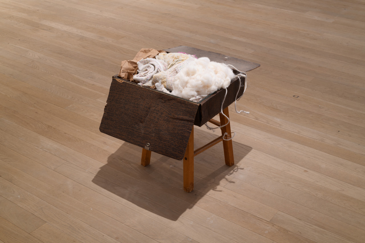 A wooden box sits open atop a stool. Fabric, string, and fluffy white material spill out.