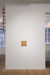 Lit from above, a square wooden panel hangs in the center of the wall. 