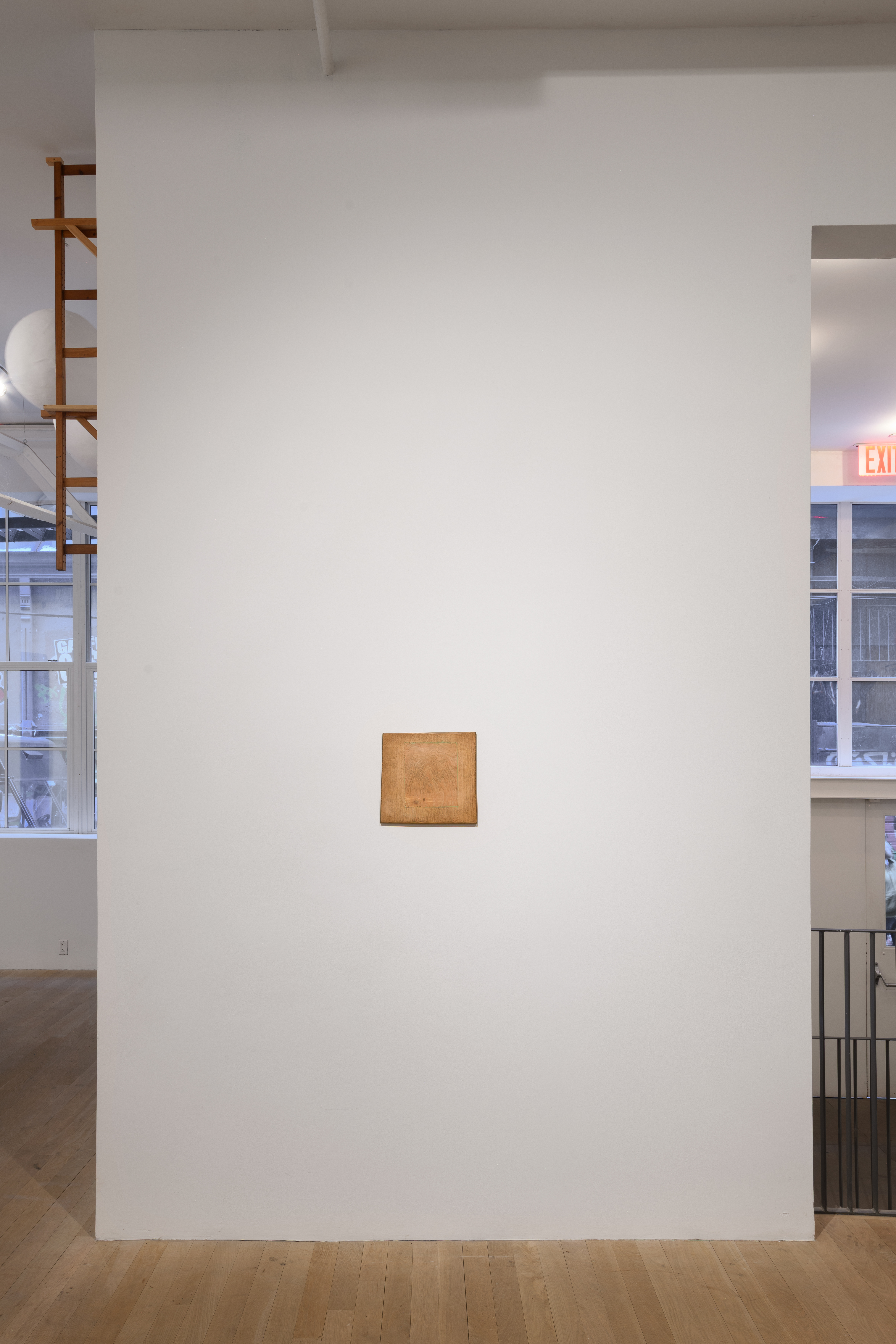 Lit from above, a square wooden panel hangs in the center of the wall. 