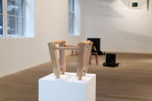 A small wooden stool is presented on a white pedestal. 