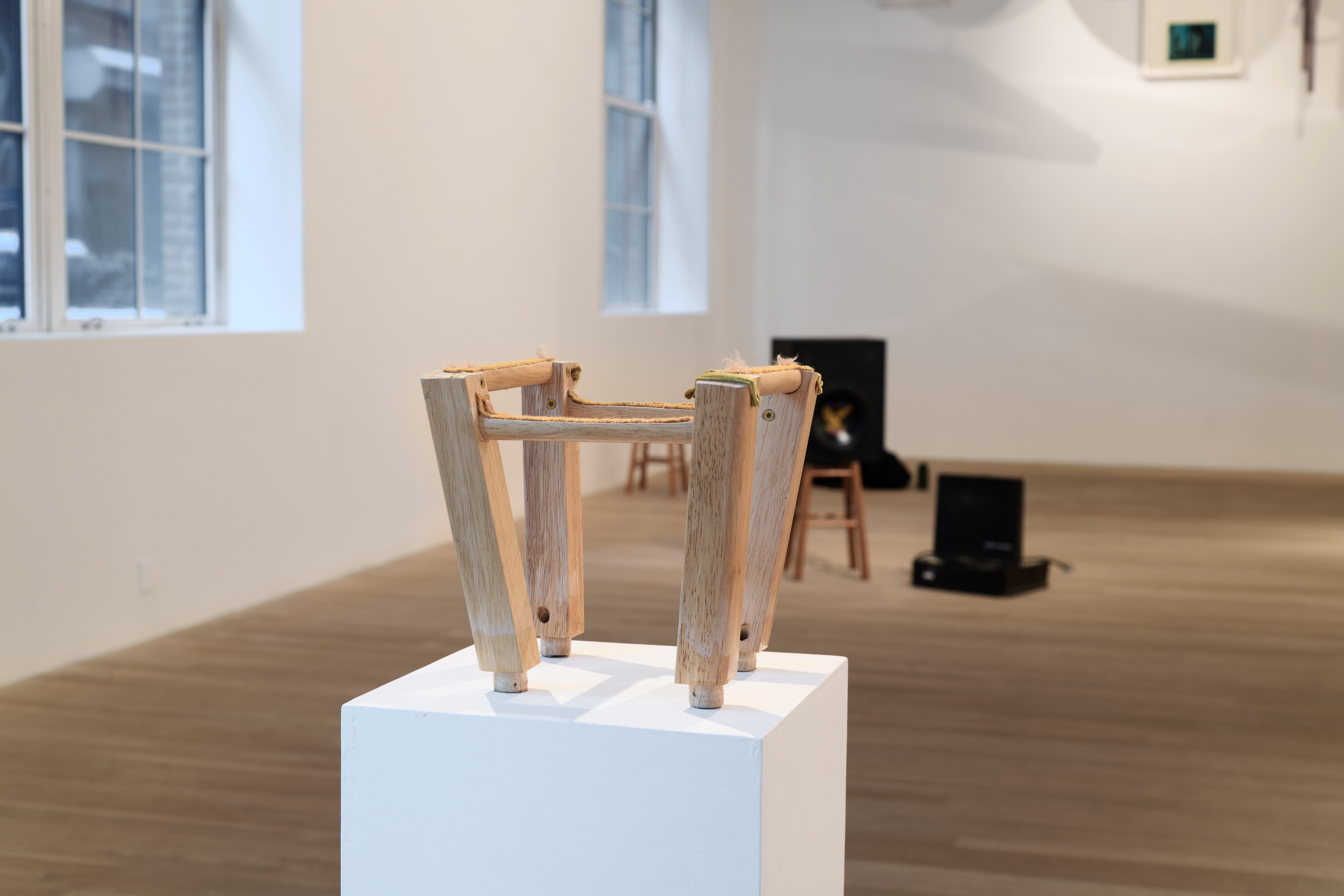 A small wooden stool is presented on a white pedestal. 