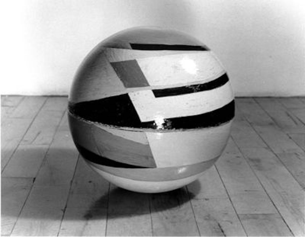 A black and white photograph of a multicolored globe sitting on a wooden floor.