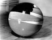 A black and white photograph of a multicolored globe sitting on a wooden floor.