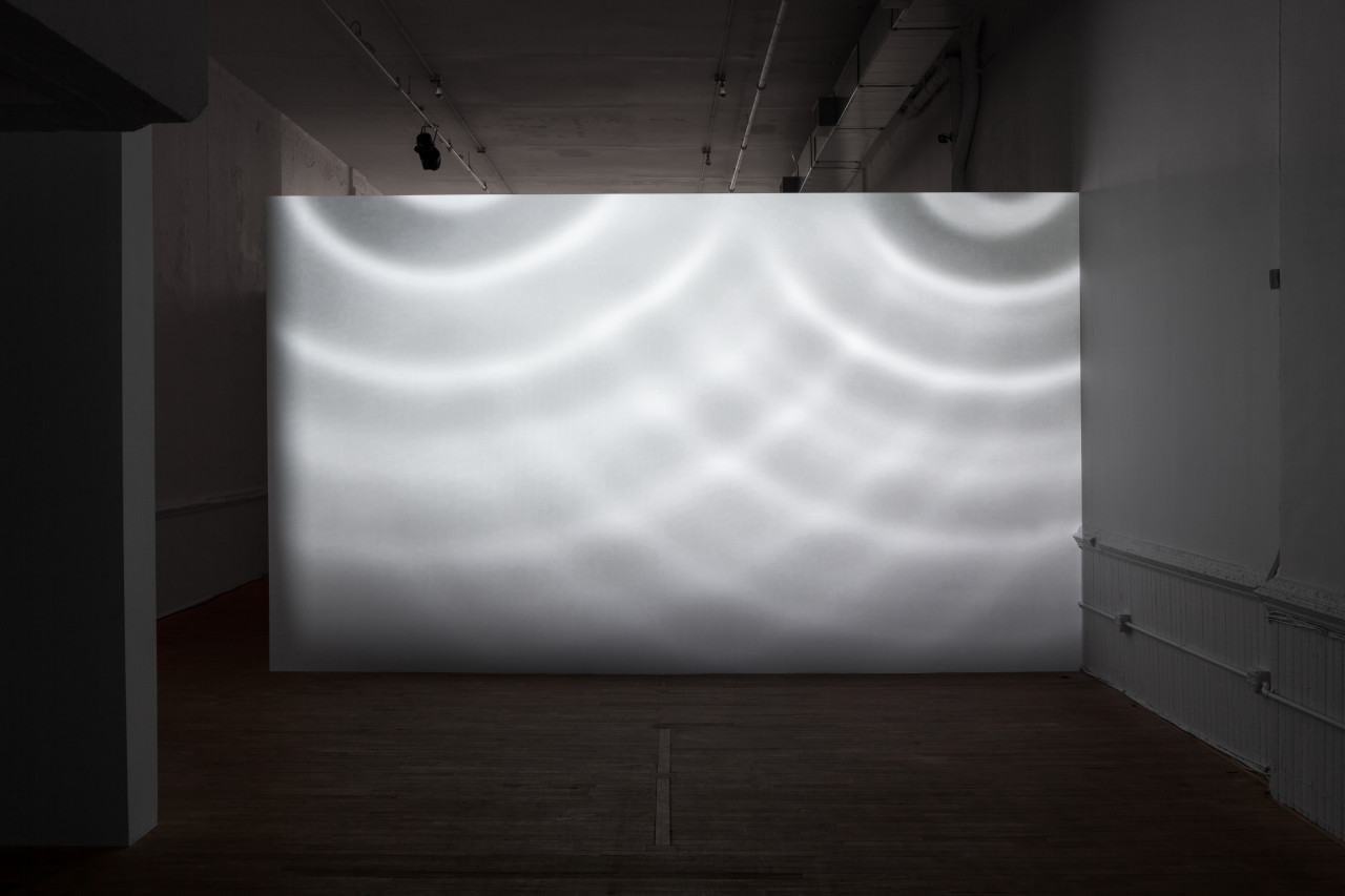 A white wall in a dimly lit room is illuminated in patterns by circles of light.