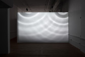 A white wall in a dimly lit room is illuminated in patterns by circles of light.