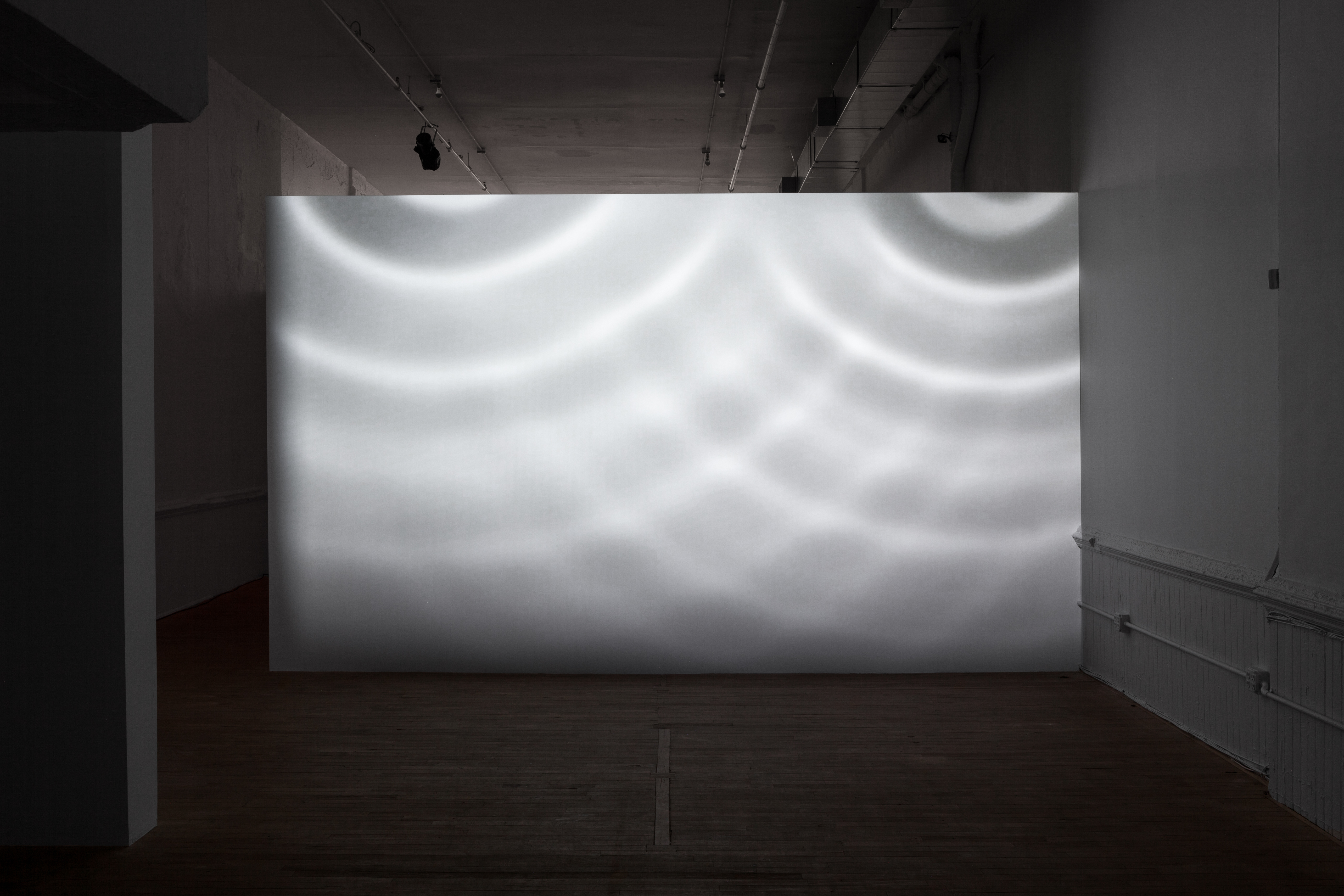 A white wall in a dimly lit room is illuminated in patterns by circles of light.