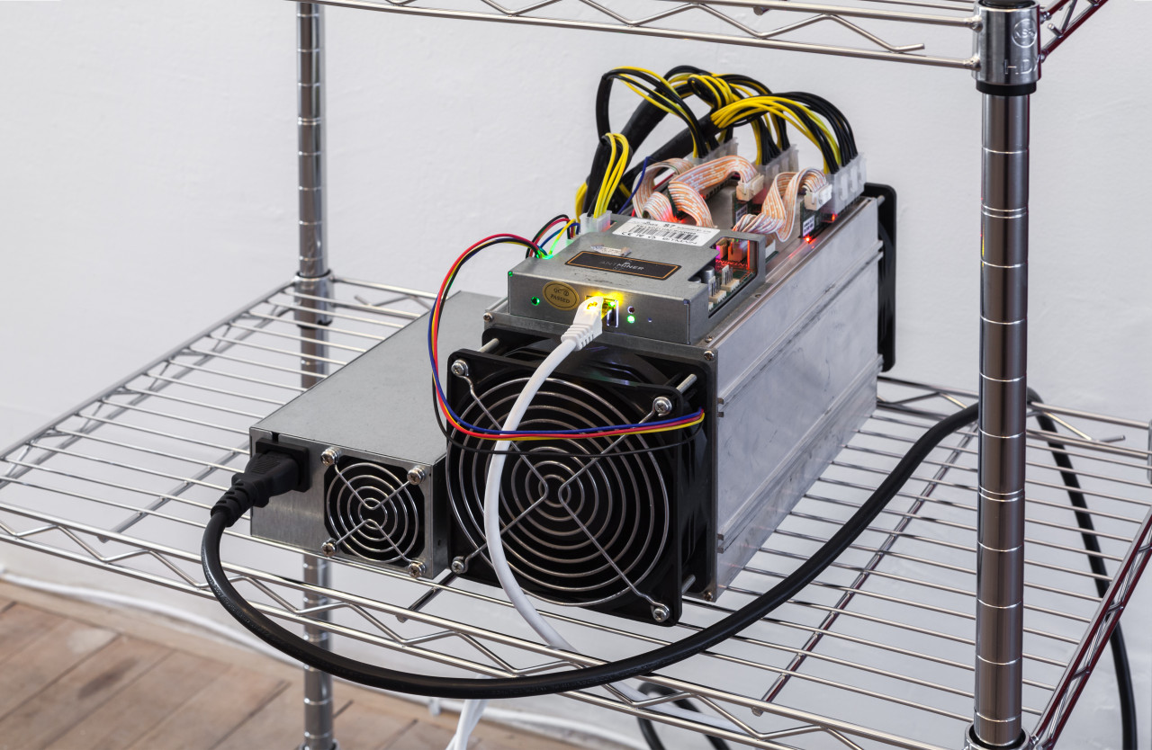 A device with several electrical wire connections is displayed on a metal wire shelf.