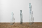 Three planks of glass lean on a white wall. Etched displays read from left to right; 