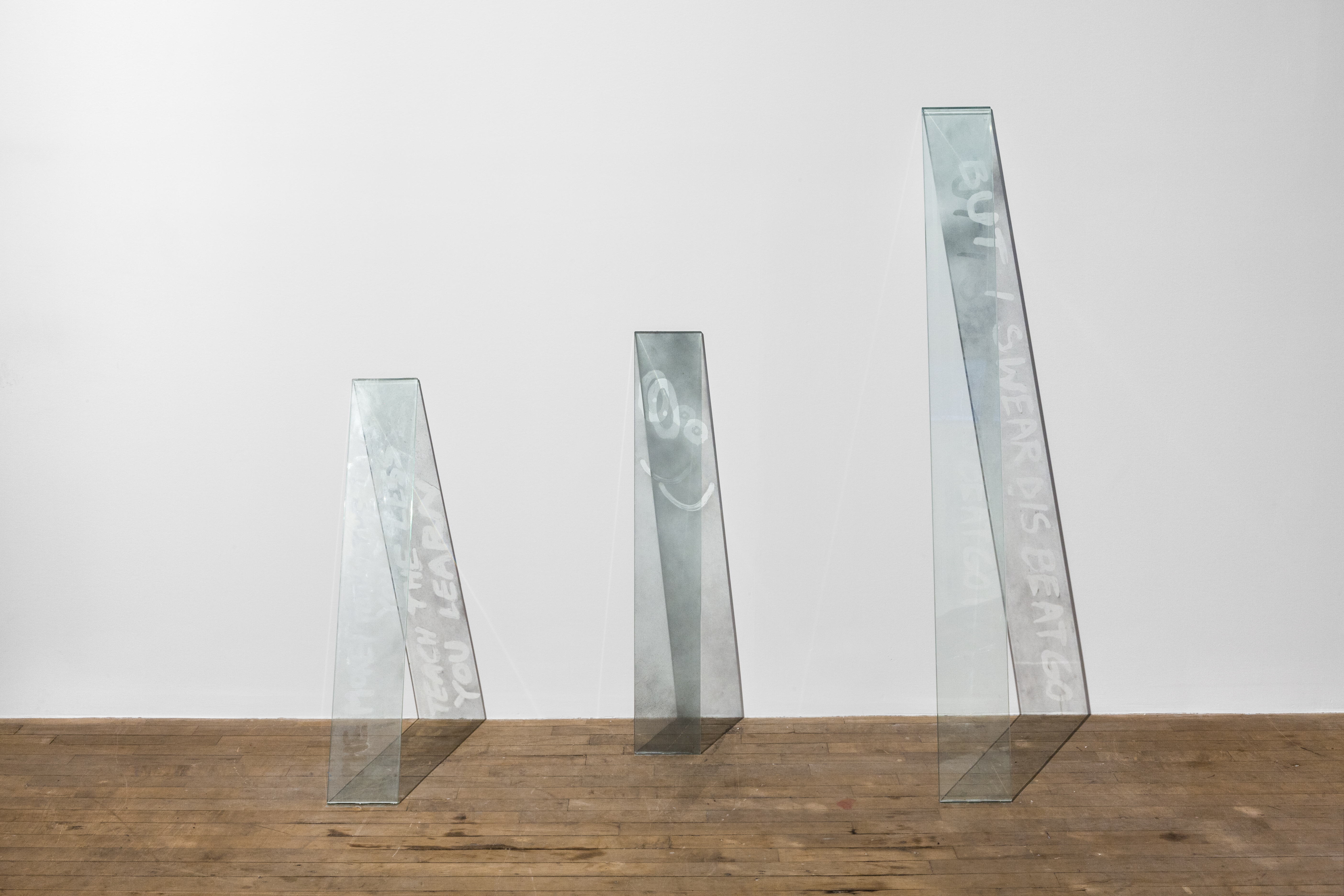 Three planks of glass lean on a white wall. Etched displays read from left to right; 