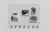Five photographs arranged in a pane of glass lean on bolts against a wall. The images in the photographs (from left to right) include a man exhaling smoke, a man looking towards the viewer, a man in a bathtub, a man, turned away from the camera, in a hospital gown, and an empty dinner plate.