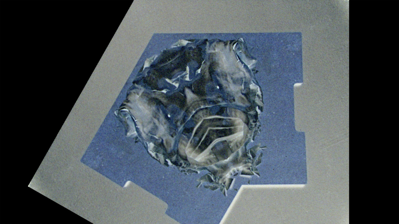 Negative film image that has been mirrored across a diagonal line of symmetry, depicting a blue board with objects arranged on it to create vaguely recognizable patterns.
