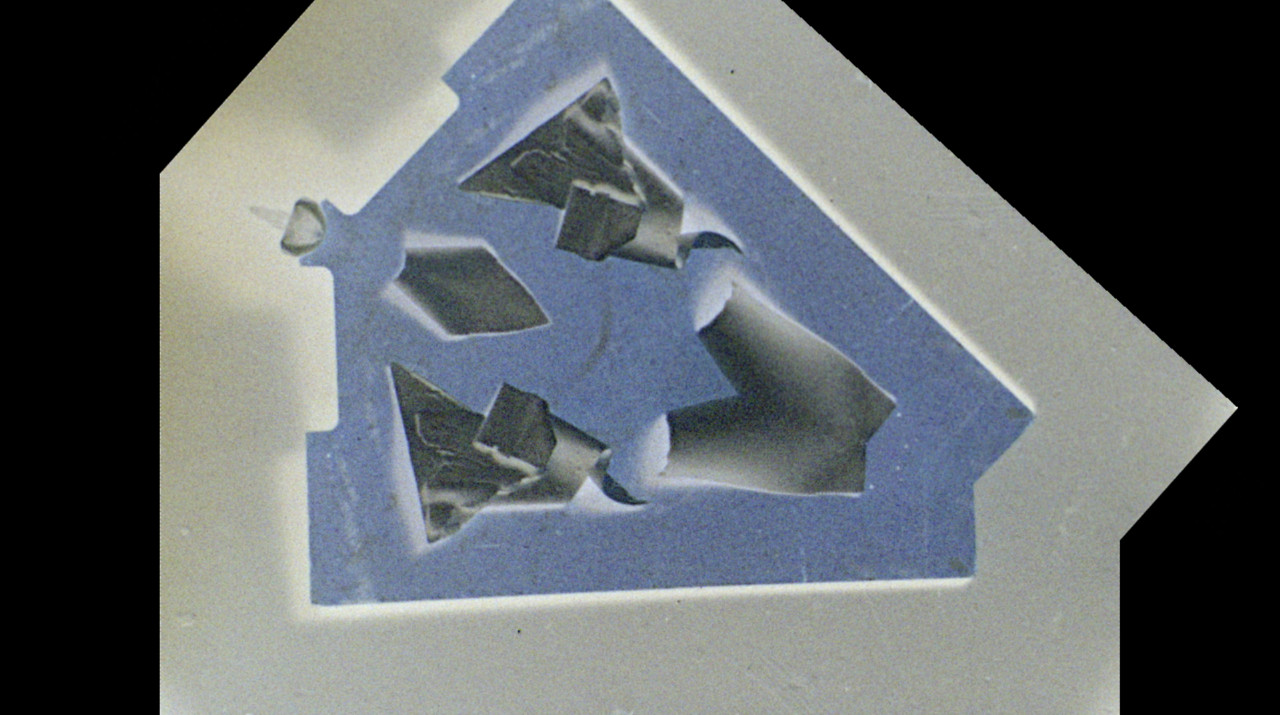 Negative film image that has been mirrored across a diagonal line of symmetry, depicting a blue board with objects arranged on it to create vaguely recognizable patterns.