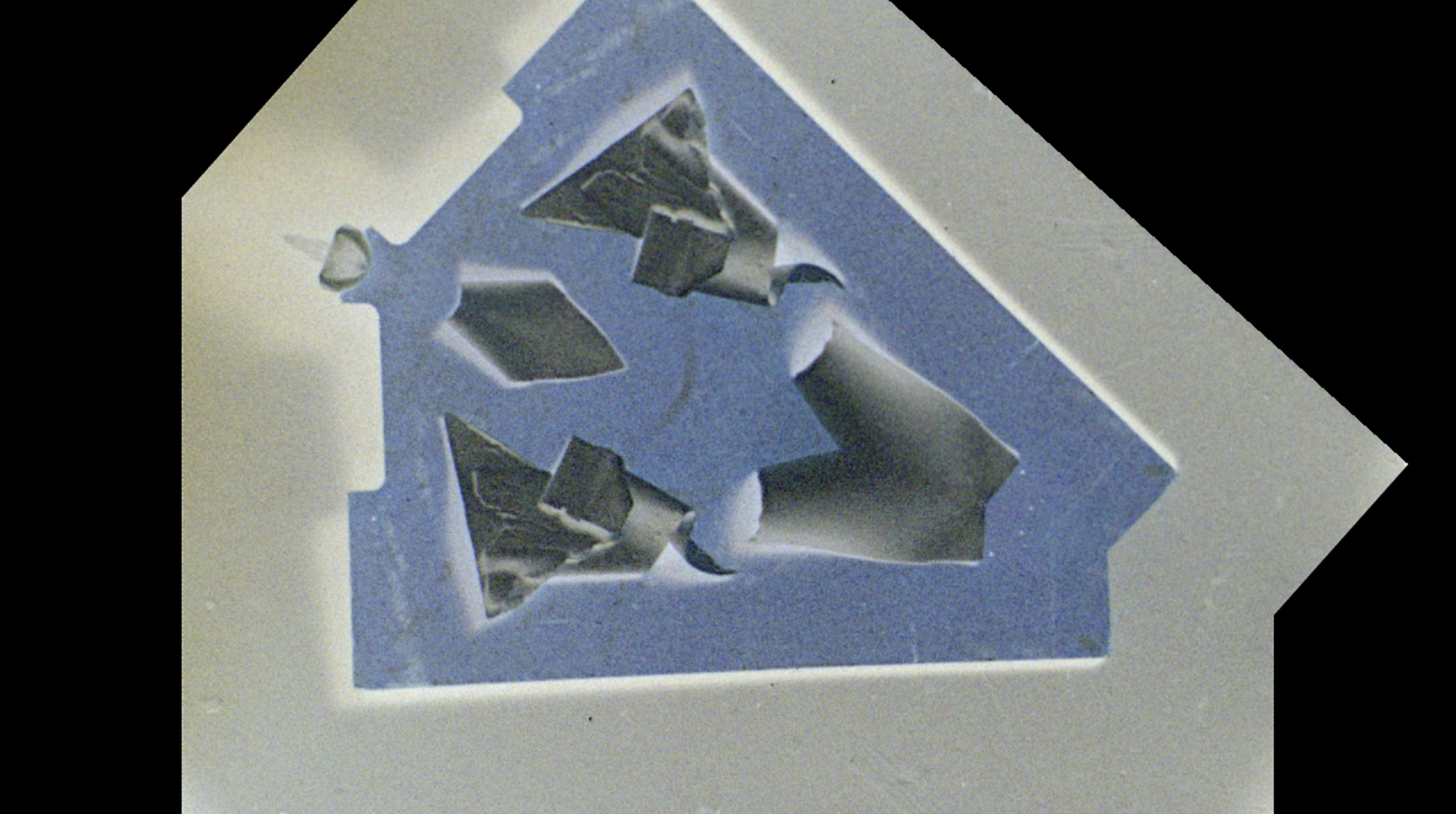 Negative film image that has been mirrored across a diagonal line of symmetry, depicting a blue board with objects arranged on it to create vaguely recognizable patterns.