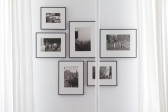 A center-parted white chiffon curtain revealing a set of six framed images mounted on the wall. A white bar runs slightly right of center of the image.