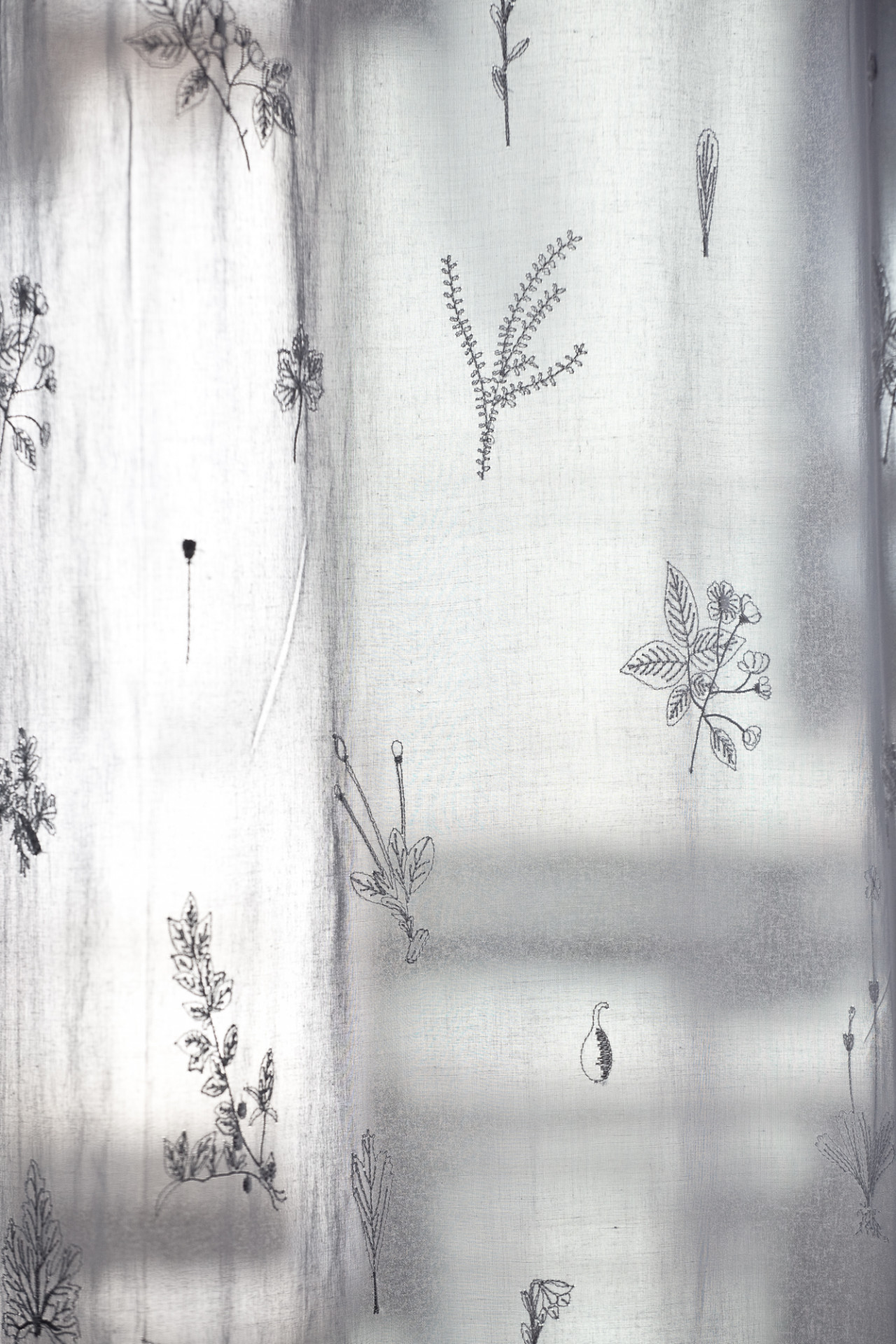 Close up of an illuminated white curtain, which reveals small, delicate embroidery of various flowers and herbs.