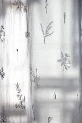 Close up of an illuminated white curtain, which reveals small, delicate embroidery of various flowers and herbs.