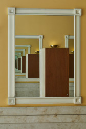 A two-toned wardrobe constructed from wood stands between two framed mirrors mounted on a yellow-orange wall above marble tiling. The reflection between the two mirrors causes the wardrobe's image to be repeated infinitely.