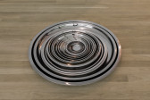 21 silver, round, stainless steel trays sit nested on a wood floor.
